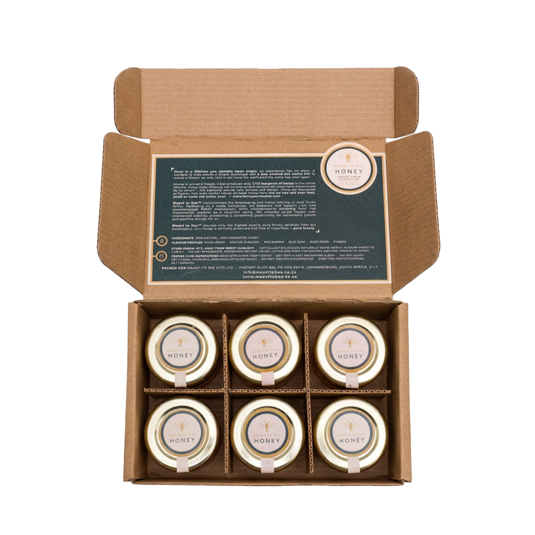 An open gift box divided into six compartments, each holding a small jar of Meant To Bee honey, seen from above.