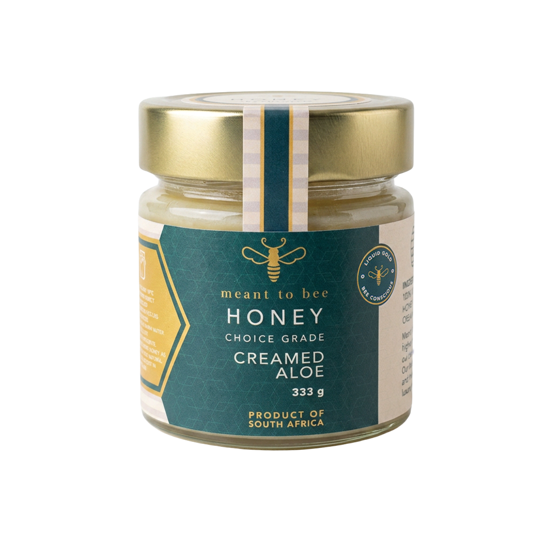 A glass jar of Meant To Bee Creamed Aloe honey, pale and opaque, with a gold lid and green label.
